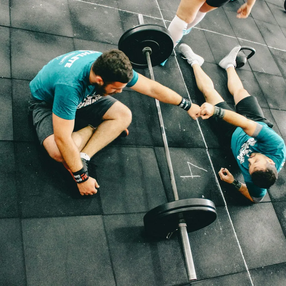 Dos deportistas chocan el puño en el suelo del gimnasio después de entrenar con barra